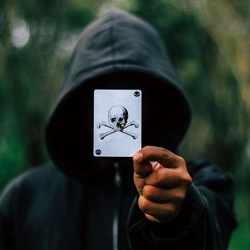 Dude in Hoodie holds up a Skull and Crossbones on a playing card.